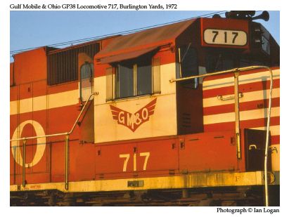 In this colour photograph taken in the Burlington Yards in 1972 by the railfan designer Ian Logan, the General Motors GP38 locomotive 717 carries the initials GM&O in white capitals on a brown background, standing for Gulf Mobile & Ohio, a railroad identified by its distinctive winged logo here painted brown on cream beneath the engineman’s window.