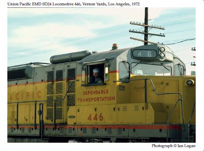 In this colour photograph taken by the railfan designer Ian Logan in 1972, an engineer wearing a blue cap smiles down from the cab of his Union Pacific EMD SD4 Locomotive 446, painted Armour Yellow with a grey roof and a slogan in red letters proclaiming Dependable Transportation. 