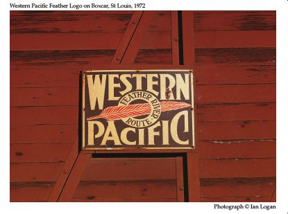 In this colour photograph taken by the railfan designer Ian Logan in St Louis in 1972, a rusting enamel sign screwed to the side of a brown-painted wooden boxcar carries the name Western Pacific in stylized white capitals on a black background. At the centre of the panel a red feather pierces a white roundel marked with Feather River Route in black seraph capitals