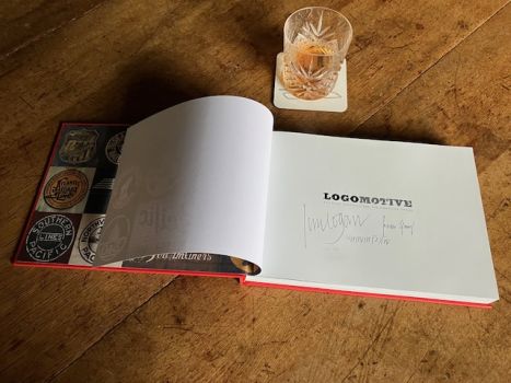 The title page of Logomotive, open beside a glass of whisky, displays the signatures of Ian Logan, Jonathan Glancey and Norman Foster.