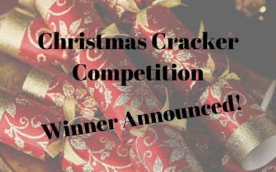 Photograph of red and gold crackers in the background, overlaid with black text announcing the winner of the Christmas Cracker Competition.