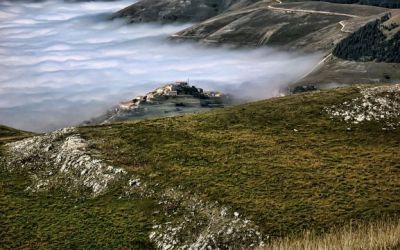 A photograph taken from a grassy mountaintop in the Marche reveals a mist-filled valley and the remote village of Castellúccio.
