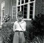 Black and white photograph of Adam Hart-Davis outside a classroom at St Andrew’s School. 