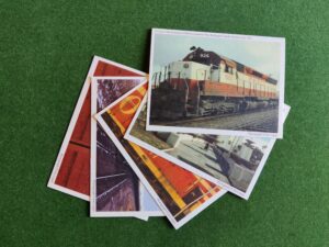 This colour image shows five railway-themed postcards on a green background arranged in a fan from top right to bottom left.