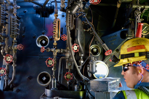 In this colour photograph taken inside the cab of Union Pacific’s Big Boy 4014 locomotive a member of the crew monitors the engineer’s controls, including the brass boiler water sight glass high up in the centre.
