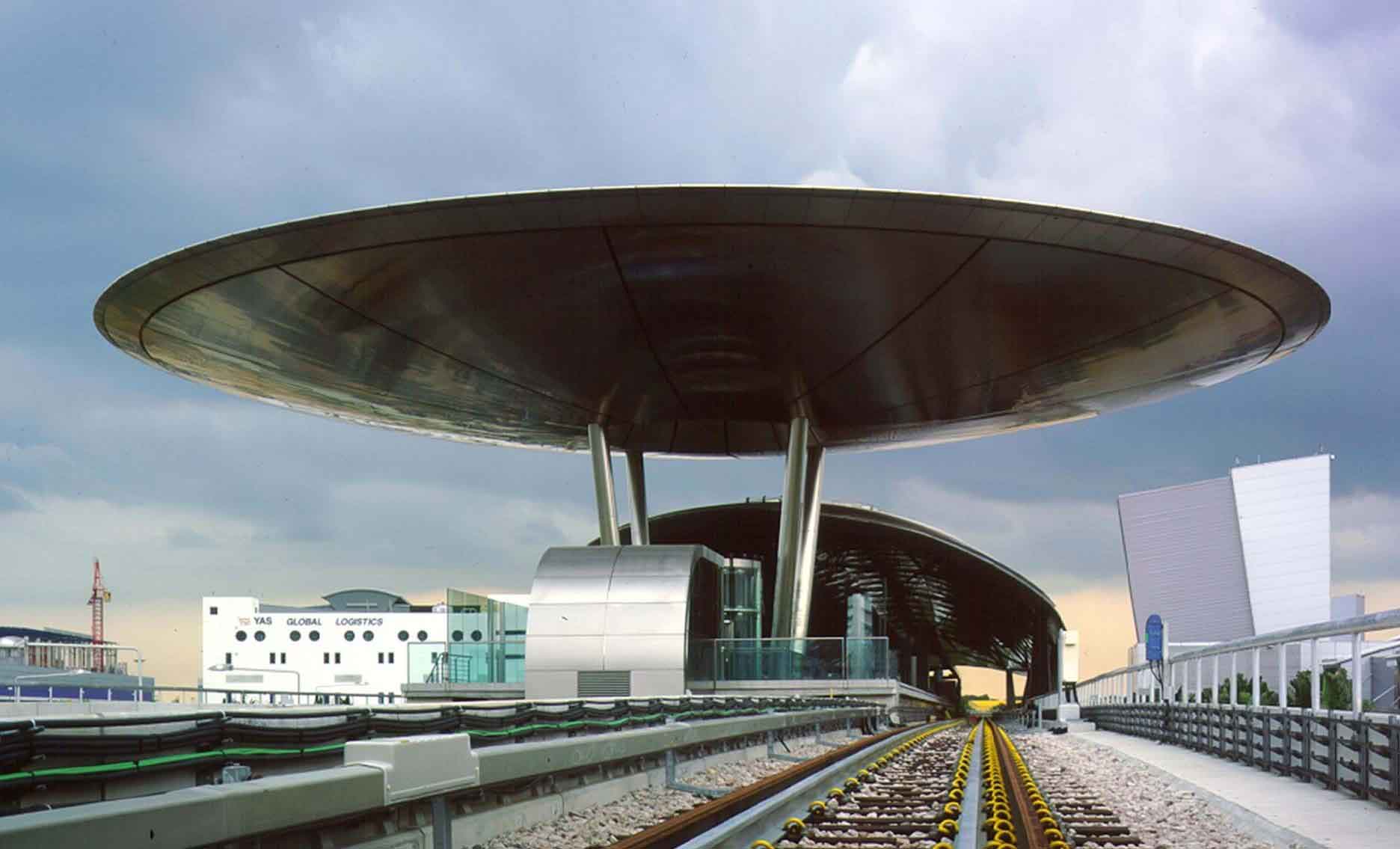 Supported on three tall struts, a disc 40 metres in diameter, sheathed in stainless steel, provides cover for the ticket hall beneath while beyond a blade-like carapace, sheathed in titanium, folds over the platforms.