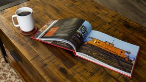 In this colour photograph, Logomotive is open at a page showing an Illinois Central Gulf caboose with a mug of coffee standing next to it to indicate the size of the book.